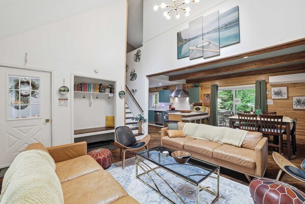 A spacious living area with a sofa, coffee table, and a dining table with chairs. There is a staircase leading to an upper level.