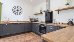 A modern kitchen with dark cabinets, a wooden countertop, a built-in oven, a microwave, and a clock on the wall. - The Goose Shed (Canterbury)