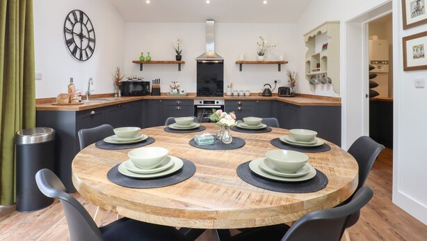A modern kitchen with a central island, built-in appliances, and a dining area with a round table set for six. - The Goose Shed (Canterbury)