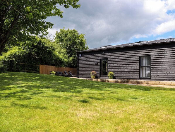 A modern log cabin with a dark exterior, a front door, and a small porch area with two potted plants. - The Goose Shed (Canterbury)