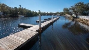 Un muelle de madera se adentra en aguas tranquilas, rodeado de árboles y un cielo despejado.