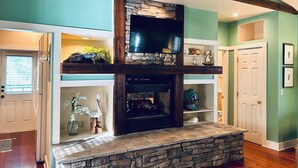 Una sala de estar con chimenea de piedra, vigas de madera, paredes color turquesa y un televisor sobre la chimenea.
