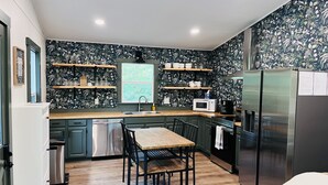 Uma cozinha moderna com papel de parede floral escuro, eletrodomésticos de aço inoxidável, bancadas de madeira e uma área de jantar com mesa e cadeiras de madeira.