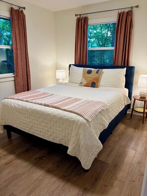A bedroom with a bed, curtains, a window, a bedside table, and a lamp. - Cozy mountain cabin in Hiawassee! (Hiawassee)