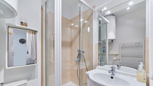 Ein modernes Badezimmer mit einer Duschkabine, einem weißen Waschbecken und einem Spiegel darüber.