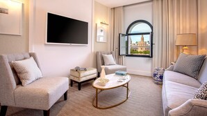 Une chambre d’hôtel équipée d’un téléviseur à écran plat, de deux fauteuils, d’un canapé, d’une table basse et offrant une vue sur un bâtiment historique par la fenêtre.