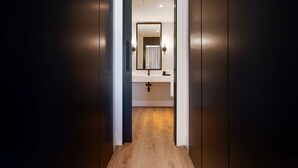 Un couloir menant à une salle de bain équipée d’un miroir, d’un lavabo et d’un porte-serviettes.