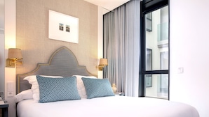 Ett hotellrum med en stor säng, två sänglampor, en sänggavel och ett fönster med gardiner.