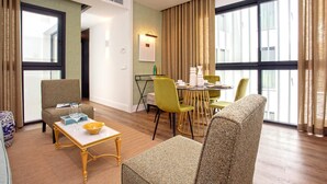 Une chambre d’hôtel moderne dotée d’un coin repas, de grandes fenêtres et d’un espace salon confortable.