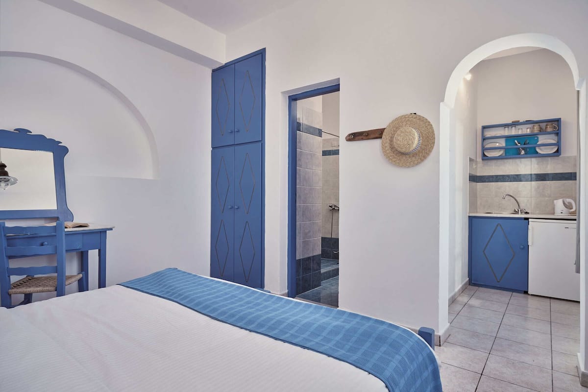 A bedroom with a bed, a desk, a wardrobe, and a bathroom visible through an open door.