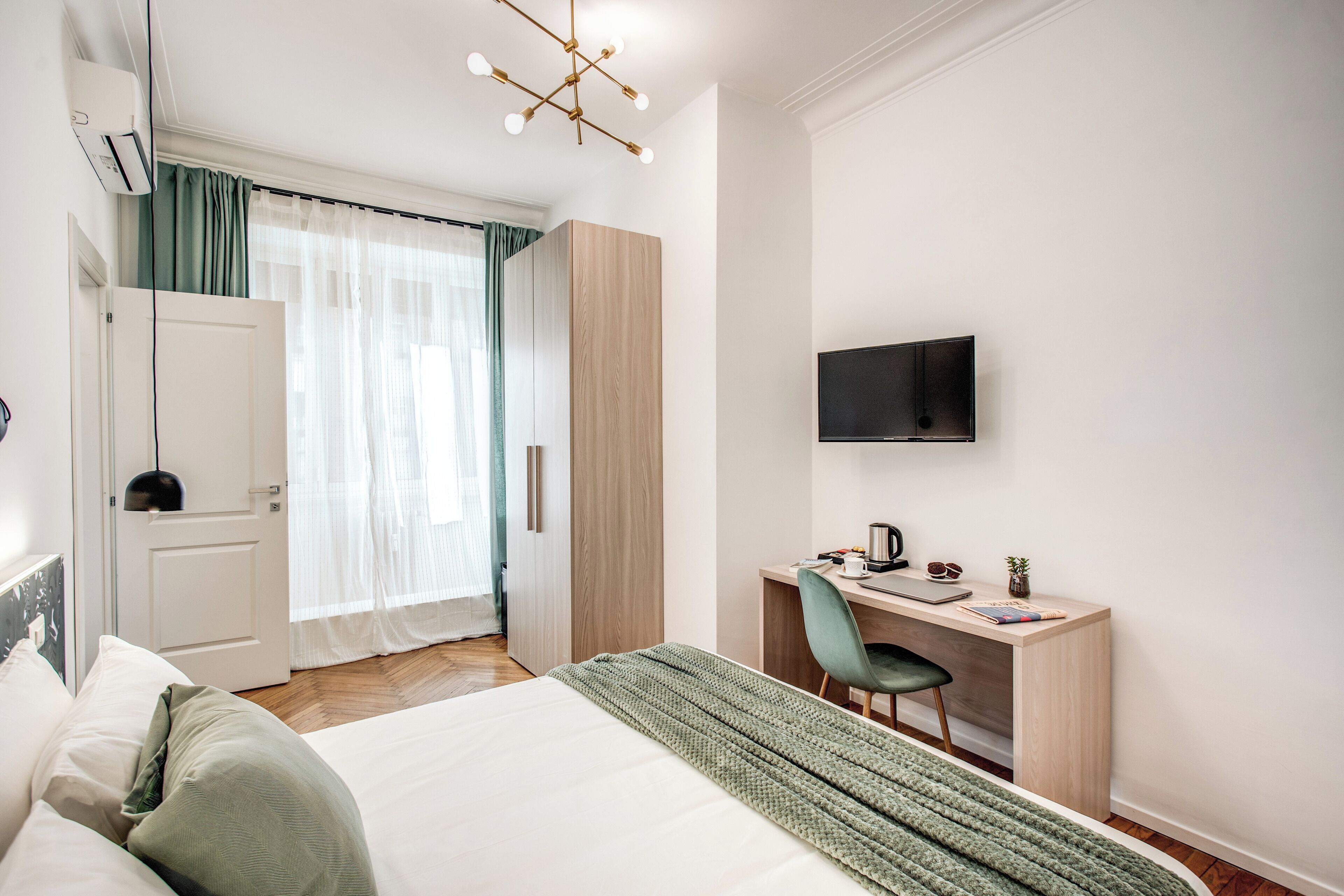A modern hotel room with a bed, a desk, a chair, a TV, and a wardrobe.