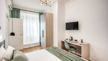 A modern hotel room with a bed, a desk, a chair, a TV, and a wardrobe.