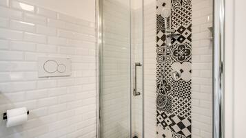 A bathroom with white subway tiles, a glass shower enclosure, and a patterned tile accent wall.