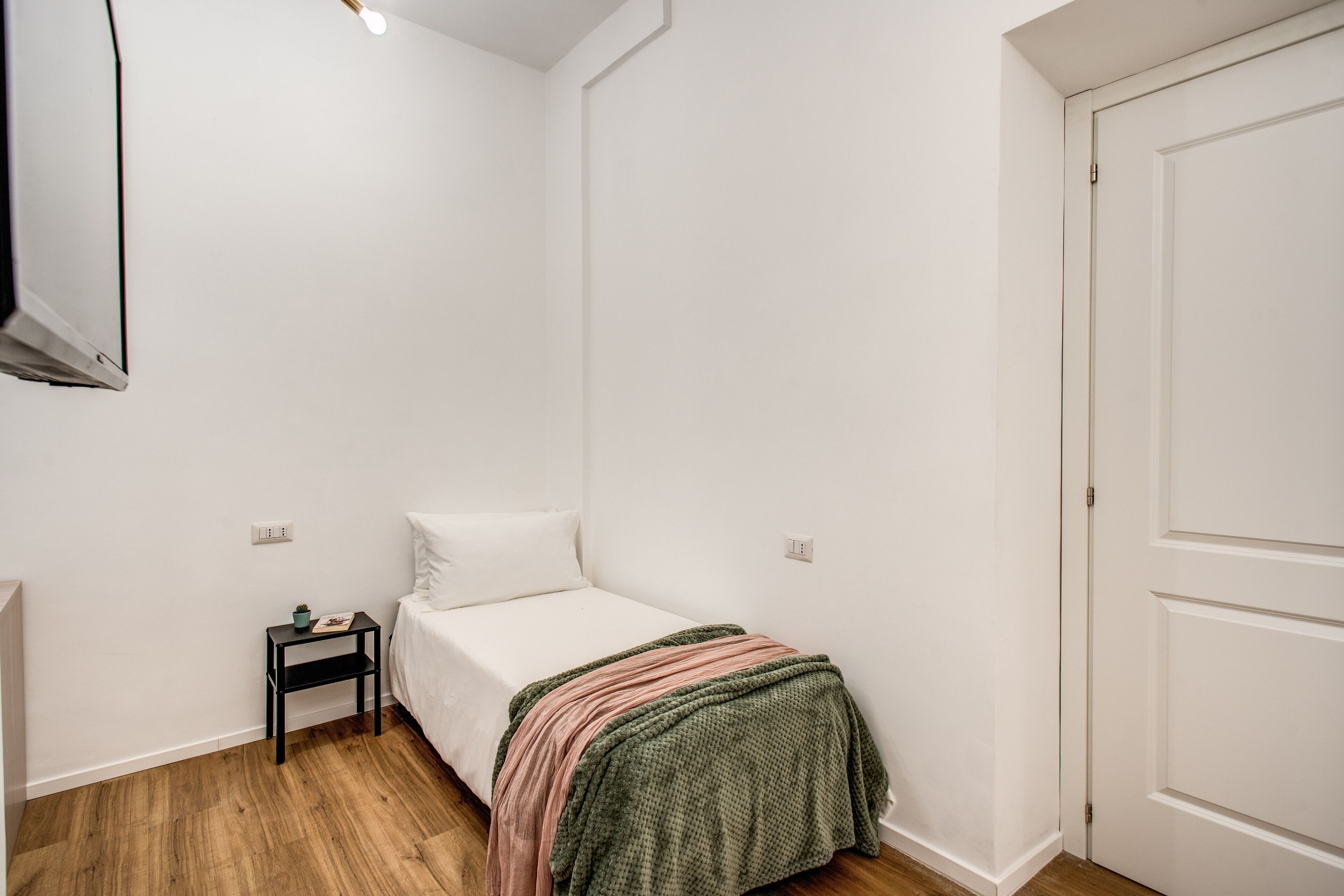 Une petite chambre à coucher, bien rangée, avec un lit simple, une table de chevet et une porte.