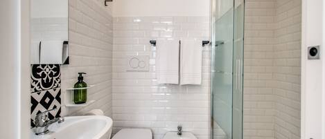 A modern bathroom with a white sink, toilet, and bidet, a glass shower enclosure, and a tiled backsplash.