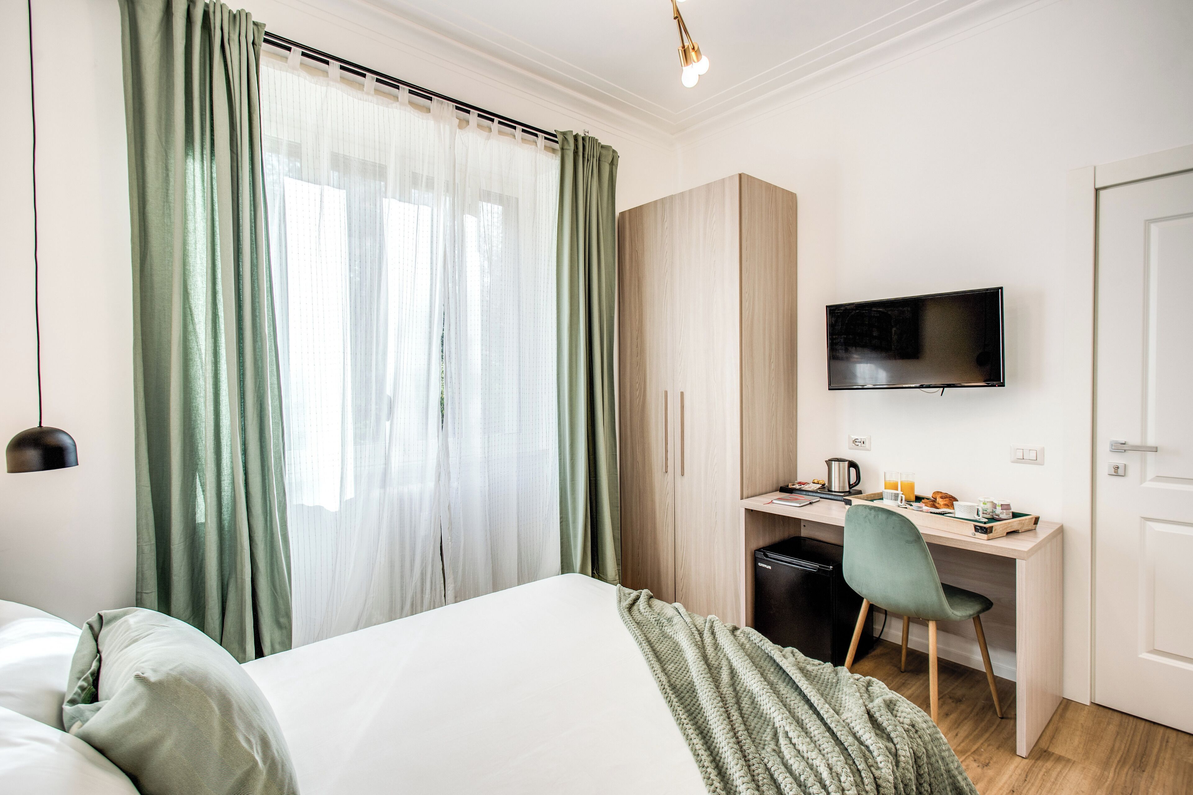 Una habitación de hotel con una cama, un escritorio con una silla, un televisor y un armario.