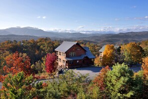 Eine Lodge mit markanter Holzarchitektur, einem überdachten Parkbereich und einem malerischen Blick auf Berge und Herbstlaub.