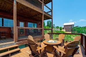 Eine Holzterrasse mit rundem Tisch und Stühlen, mit Blick auf eine bewaldete Gegend.