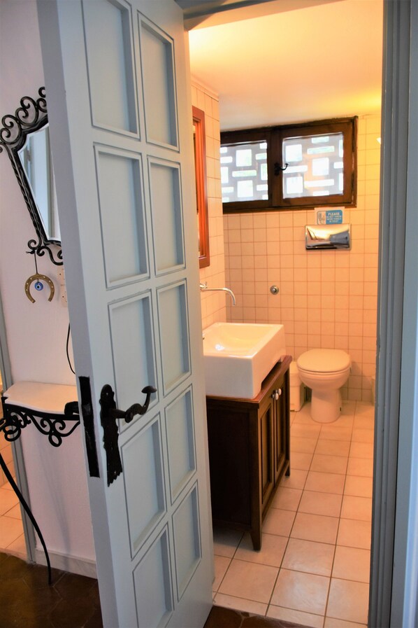 A bathroom with a white sink, a toilet, and a window with blinds. - Villa Anthi (Skiathos)