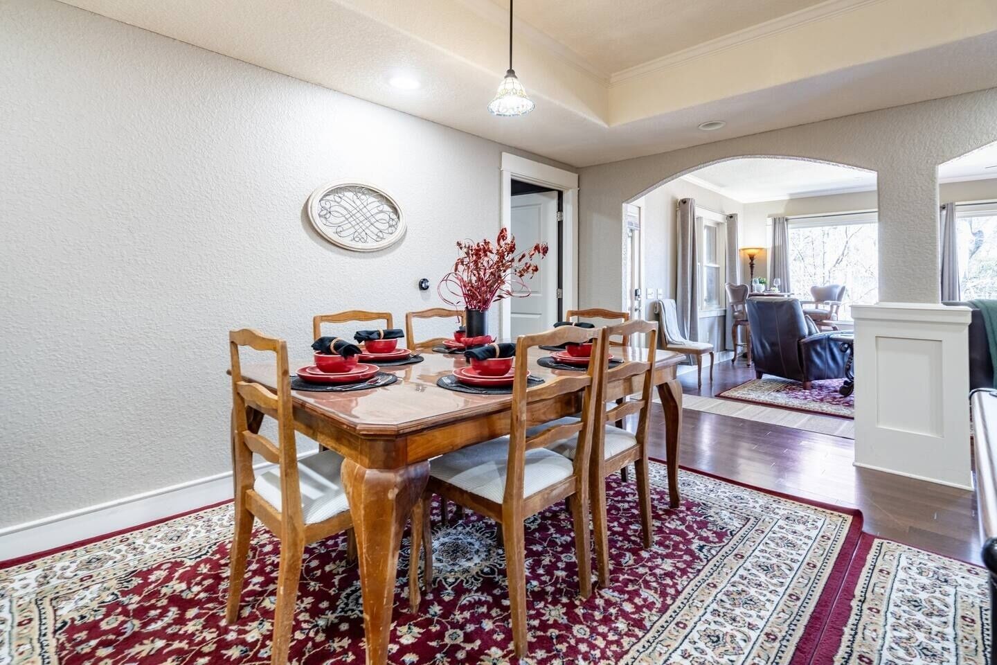 Un comedor con una mesa de madera dispuesta para seis personas, rodeada de sillas, y una alfombra estampada en el suelo.