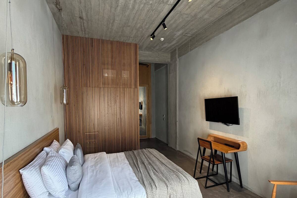 A modern bedroom with a wooden bed, a desk, and a television.