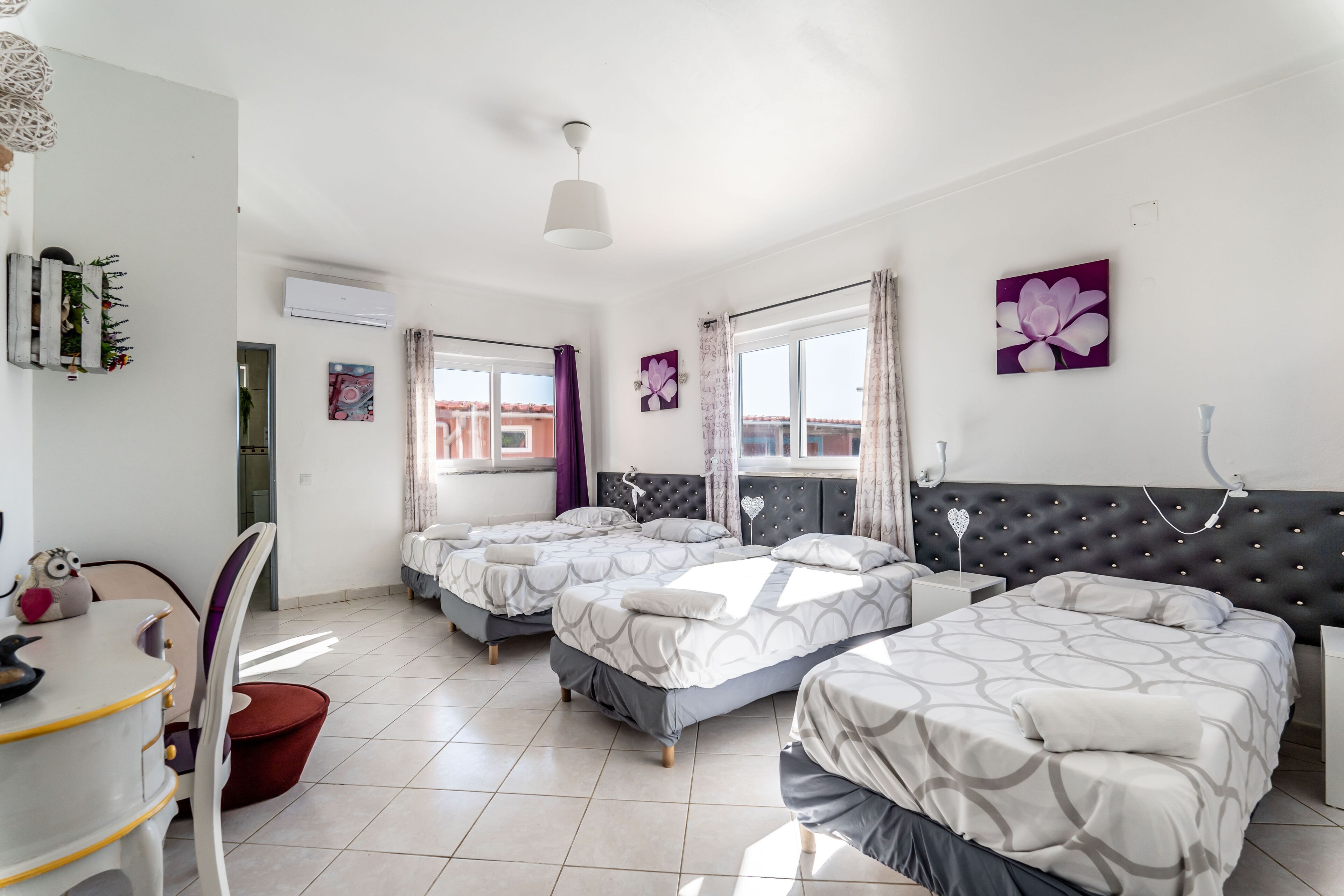 A hotel room with three beds, a dining area, and a view of the city.