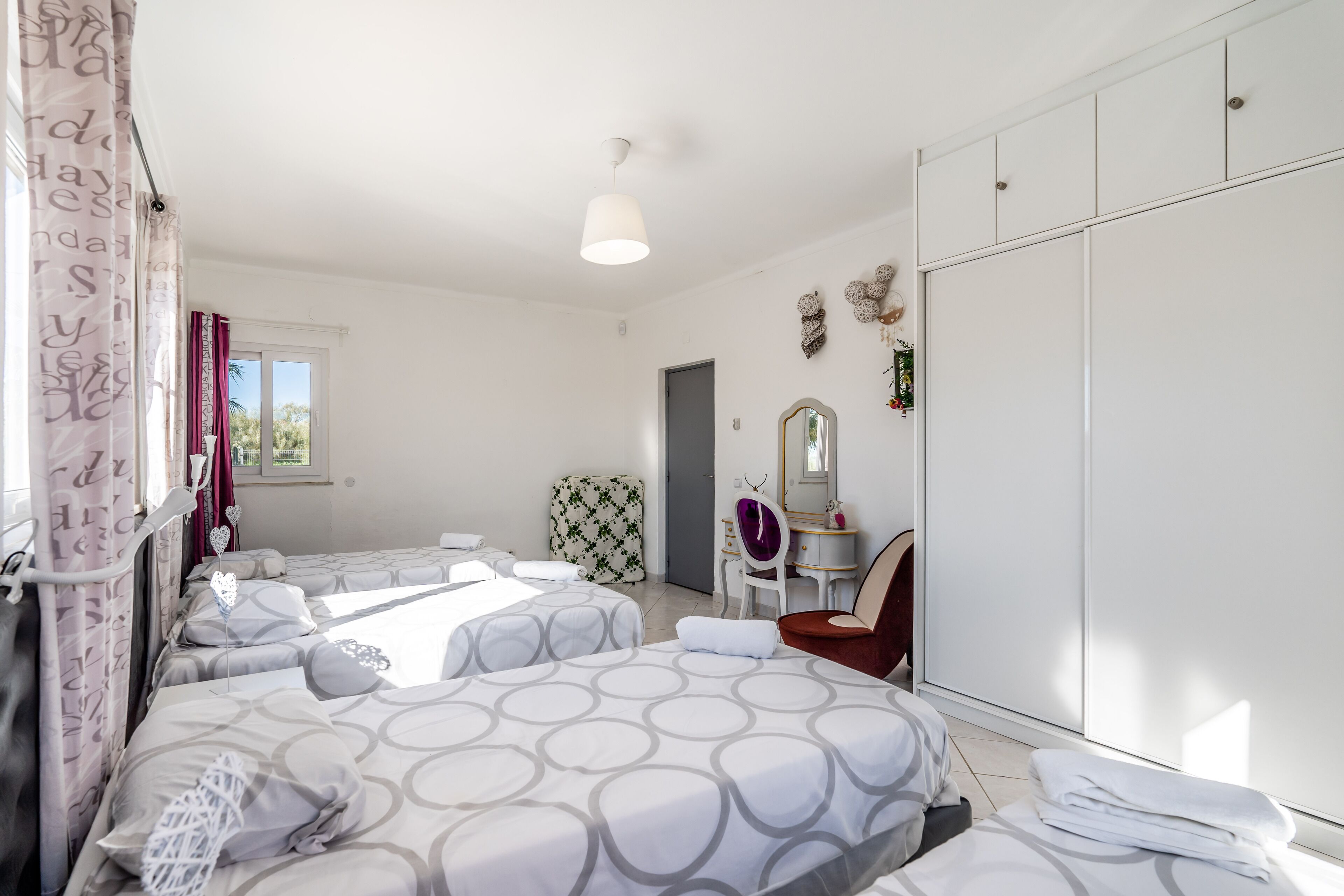 A hotel room with two beds, a desk, a chair, a wardrobe, and a window.