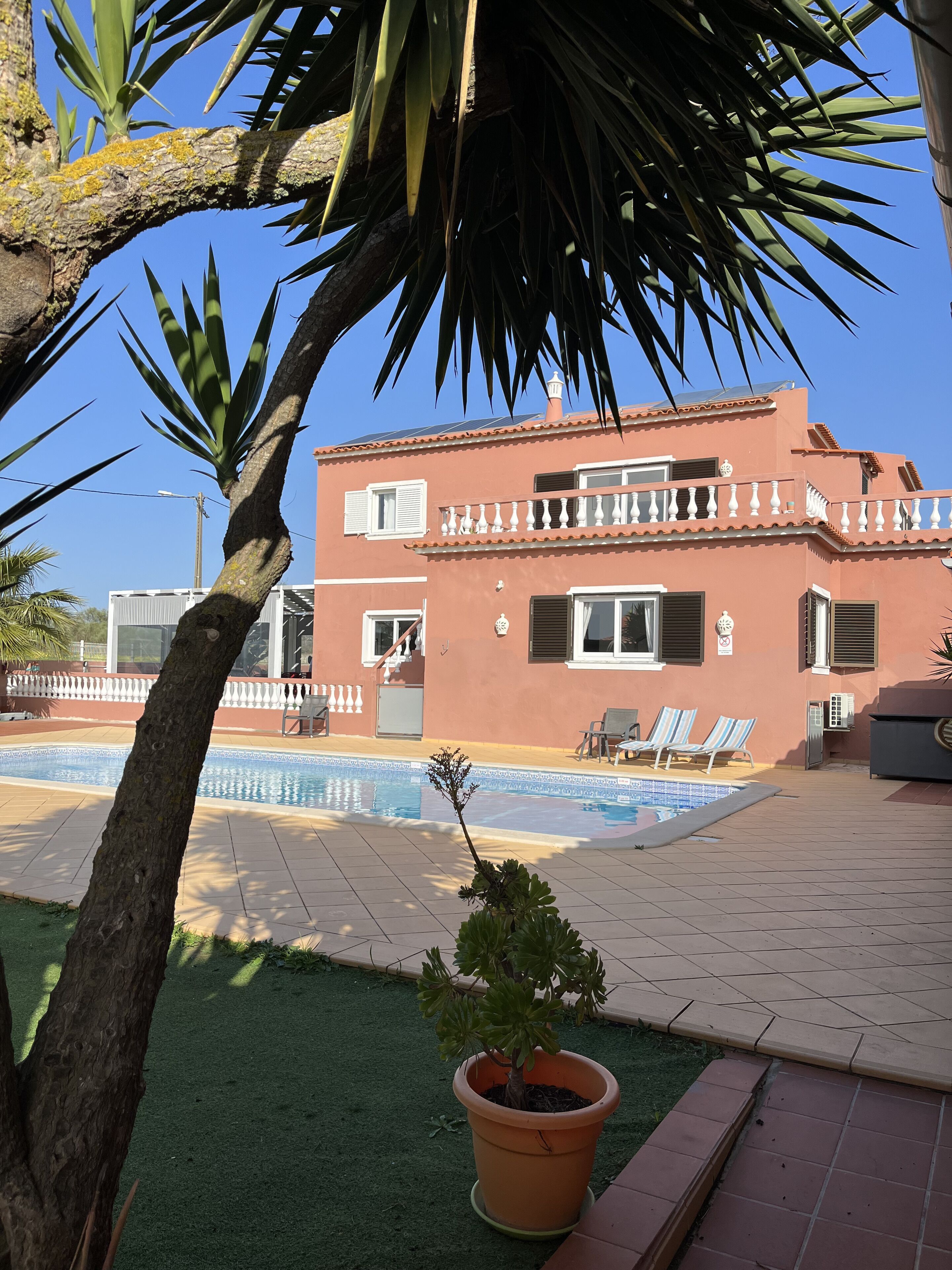 Un edificio de dos pisos con piscina, mobiliario exterior y una planta en maceta.