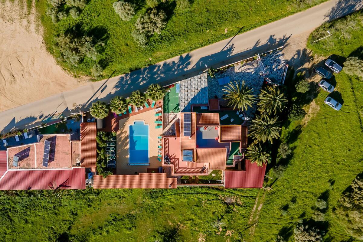 An aerial view of a resort with a swimming pool, multiple guest rooms, and a beach access road.