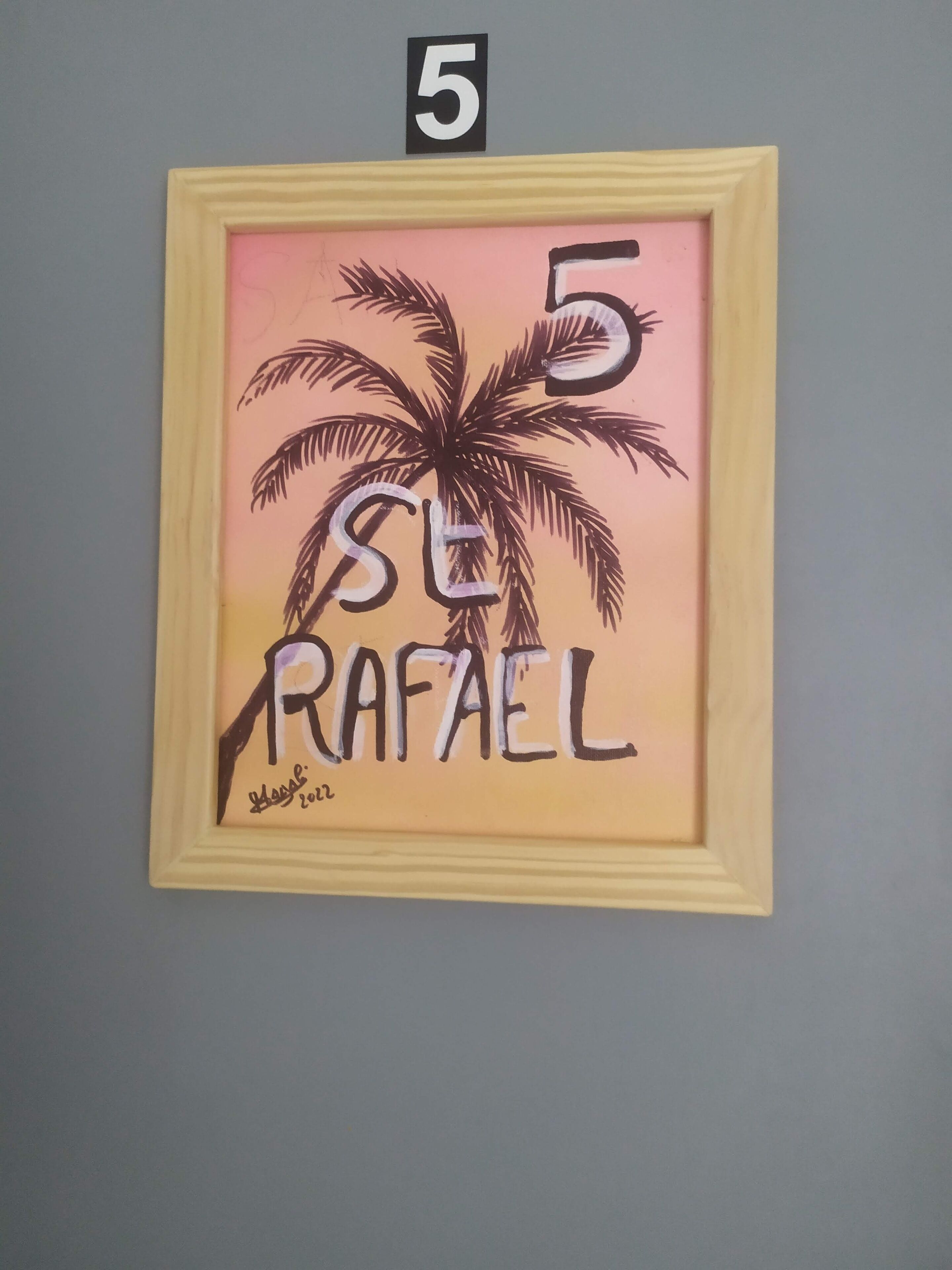 A framed artwork with a palm tree and the name "SE RAFAEL" on a wall.