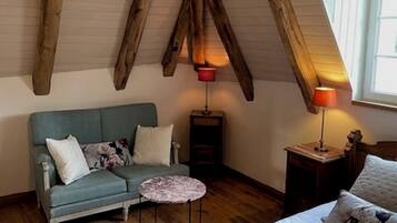A cozy attic bedroom with exposed wooden beams, a bed, a sofa, and two small tables.