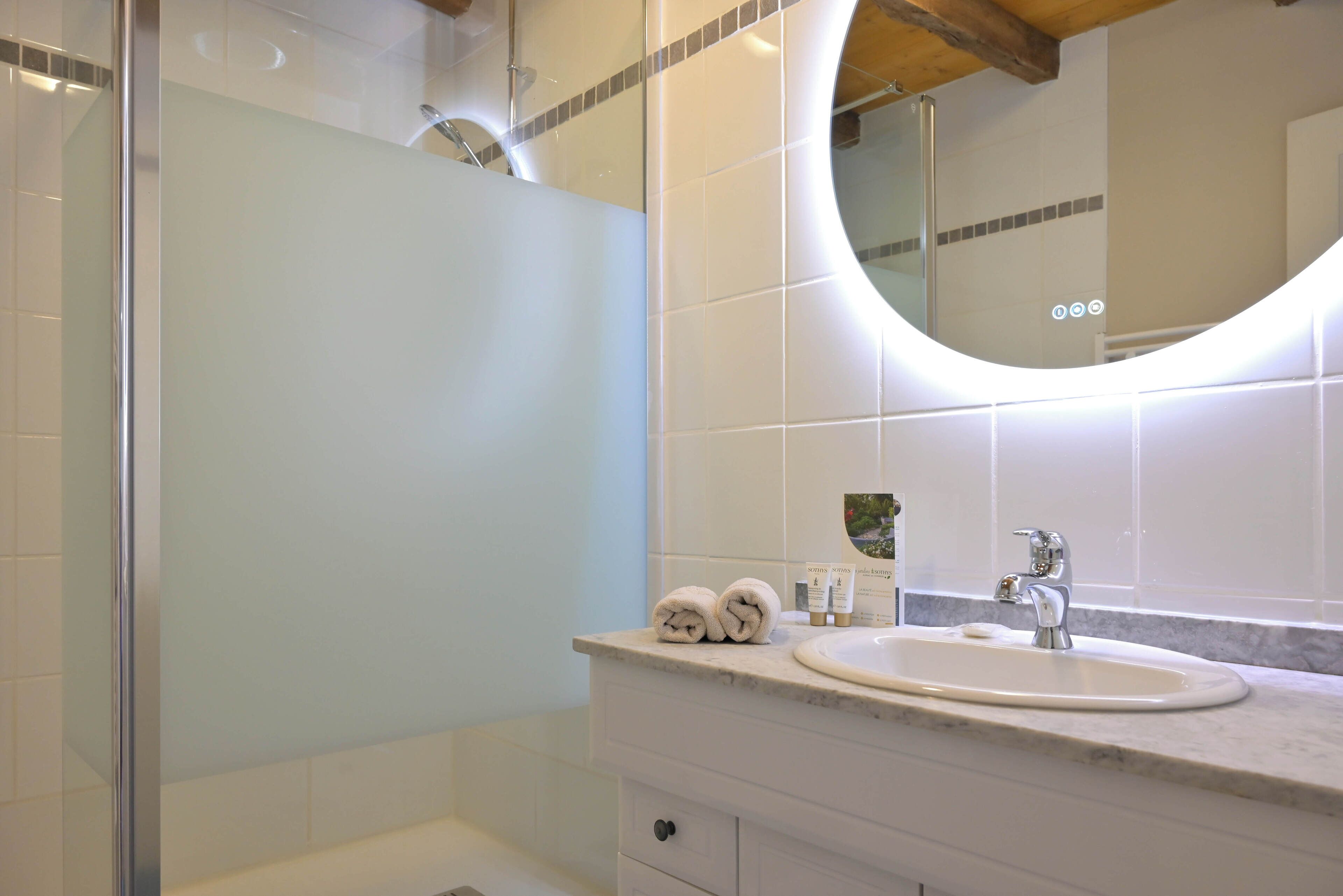 A bathroom with a glass shower enclosure, a sink with a mirror above it, and a towel rack with towels.