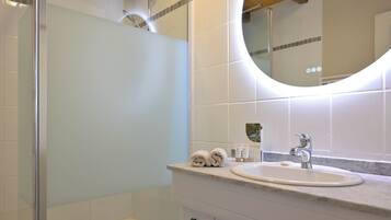A bathroom with a glass shower enclosure, a sink with a mirror above it, and a towel rack with towels.