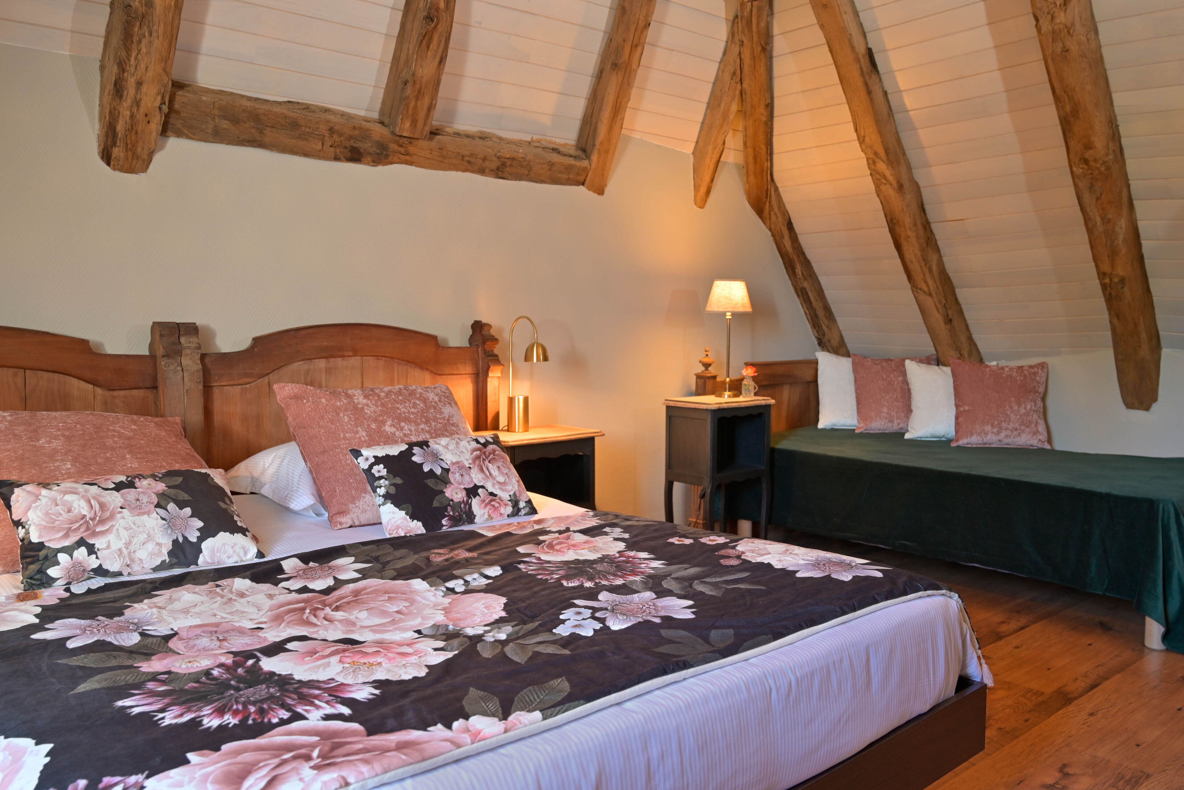 Un dormitorio con techo de madera, una cama con ropa de cama floral, mesitas de noche y una lámpara.