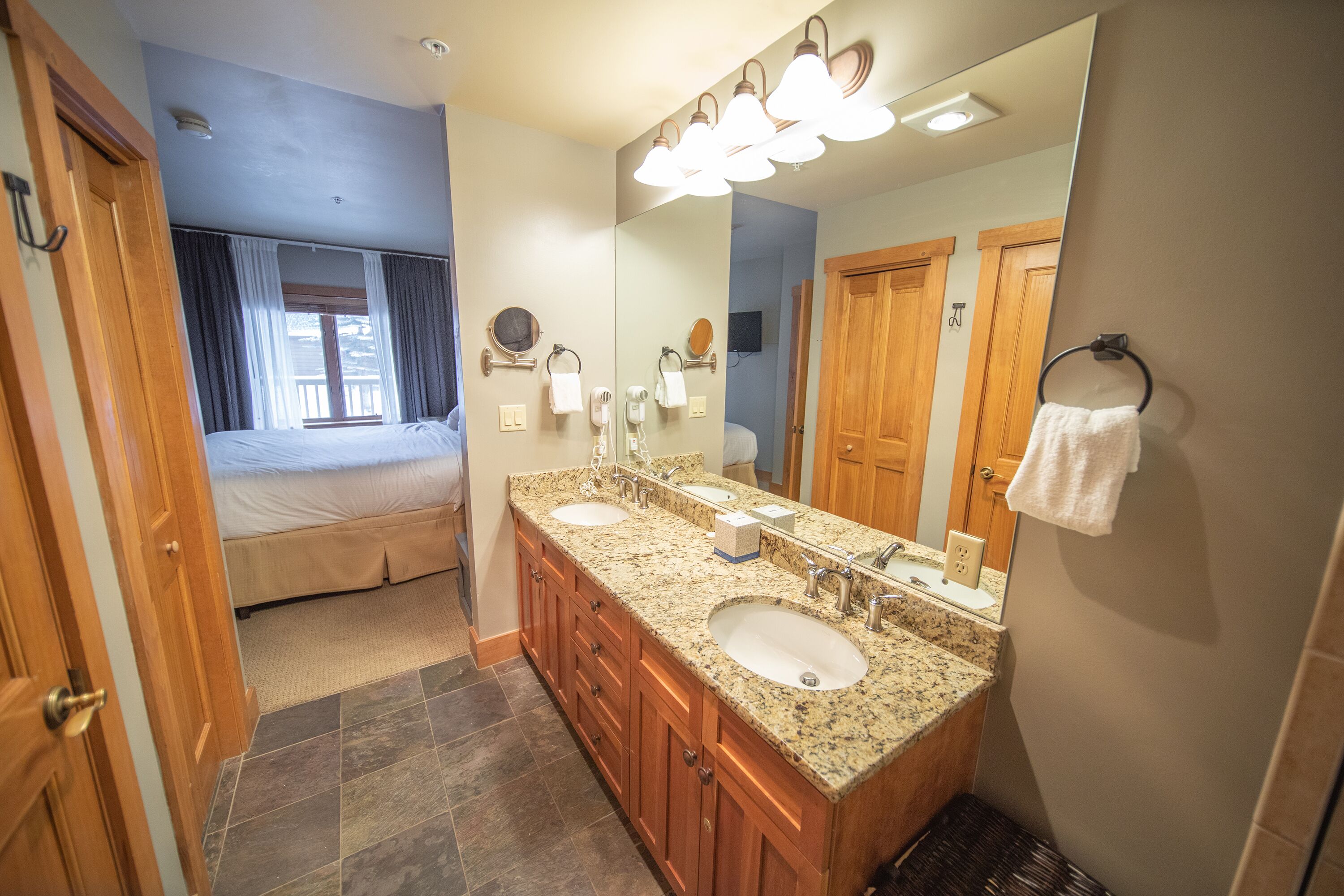 A bathroom with a double sink vanity, a large mirror, and a wooden door.