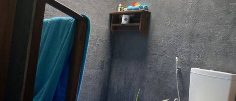 A compact bathroom with a blue floor, a white toilet, a small shelf with toiletries, and a potted plant.