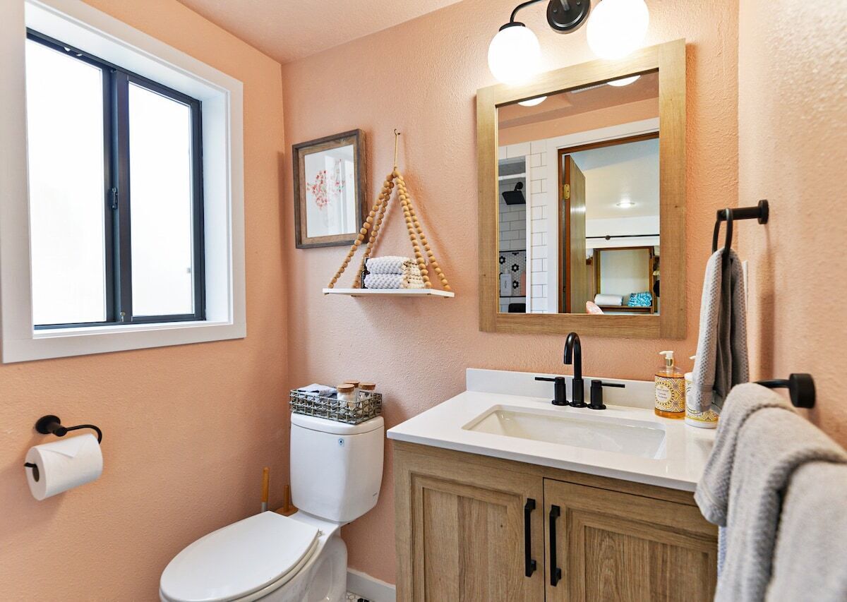 A bathroom with a toilet, sink, wooden cabinets, a hanging towel rack, and a window.