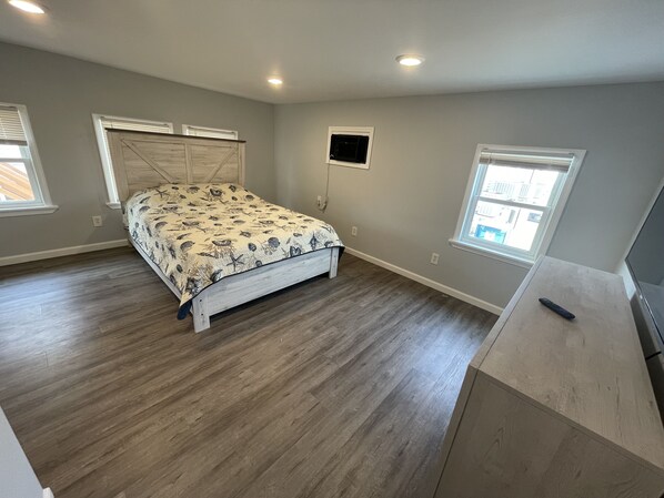 Une chambre à coucher avec un lit, un plancher en bois, une télévision et deux fenêtres.