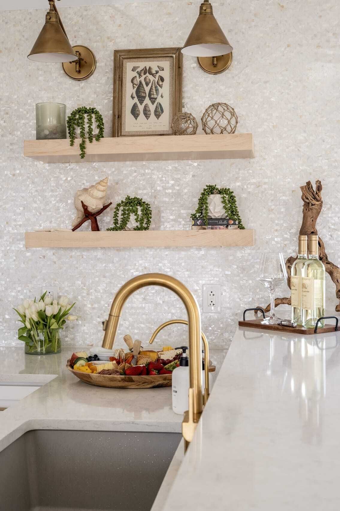 A kitchen with a white marble backsplash, wooden shelves with decorative items, a gold faucet, and a fruit bowl.
