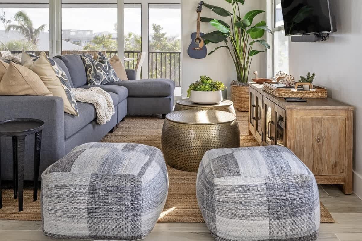 A living room with a grey sofa, two ottomans, a wooden cabinet, and a TV mounted on the wall.