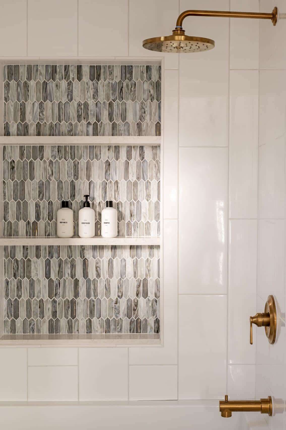 A bathroom with a shower, a marble-patterned wall, and a shelf with toiletries.