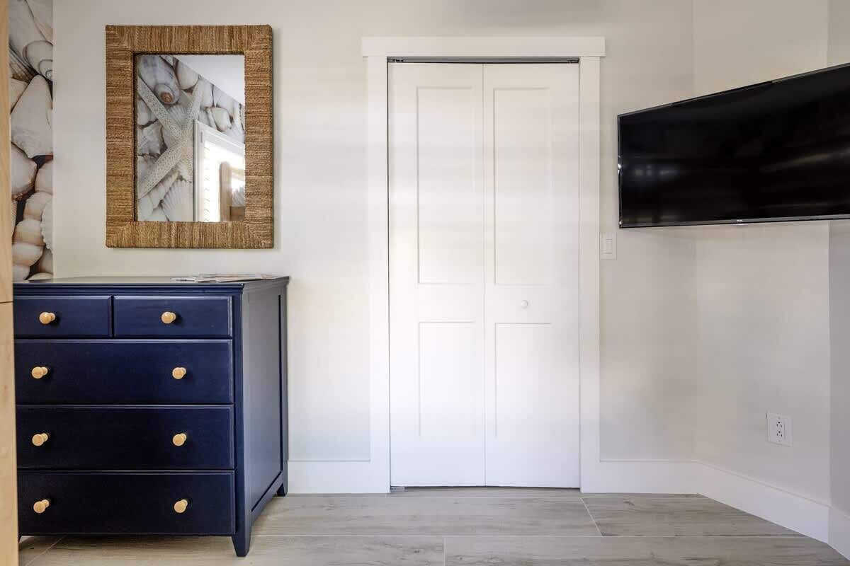 A room with a dark blue dresser with wooden knobs, a white door, and a mounted flat-screen TV on the wall.