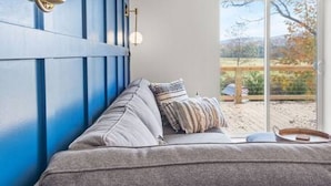 A modern living room with a grey sofa, blue accent wall, and a view of a garden through large windows.