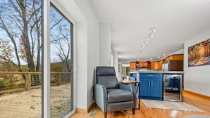 A modern interior with a large sliding glass door leading to a deck, a dining area with a table and chairs, and a kitchen with blue cabinets and a refrigerator.