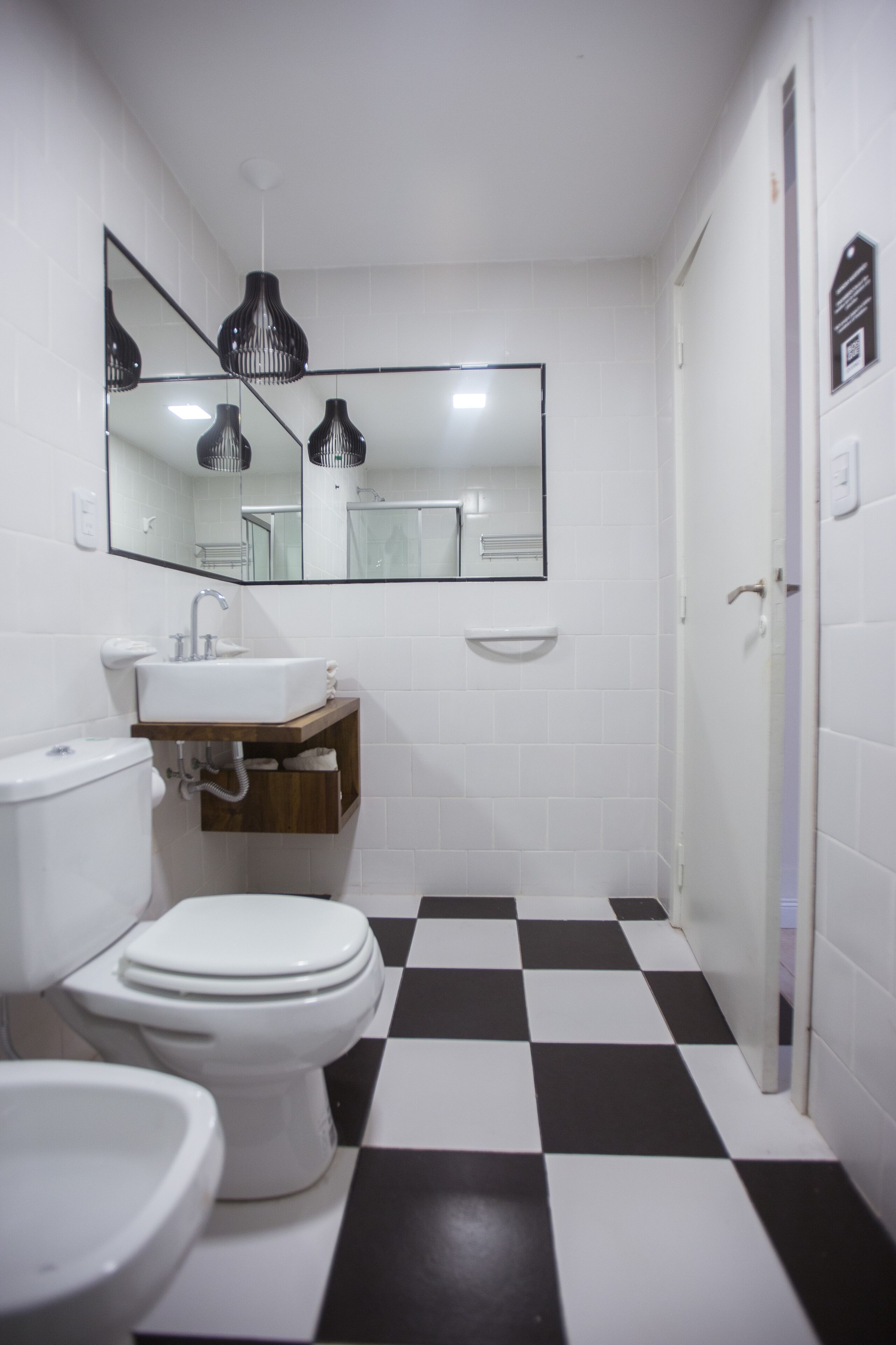 A bathroom with a white sink, toilet, and bidet, a mirror above the sink, and a black and white checkered floor.