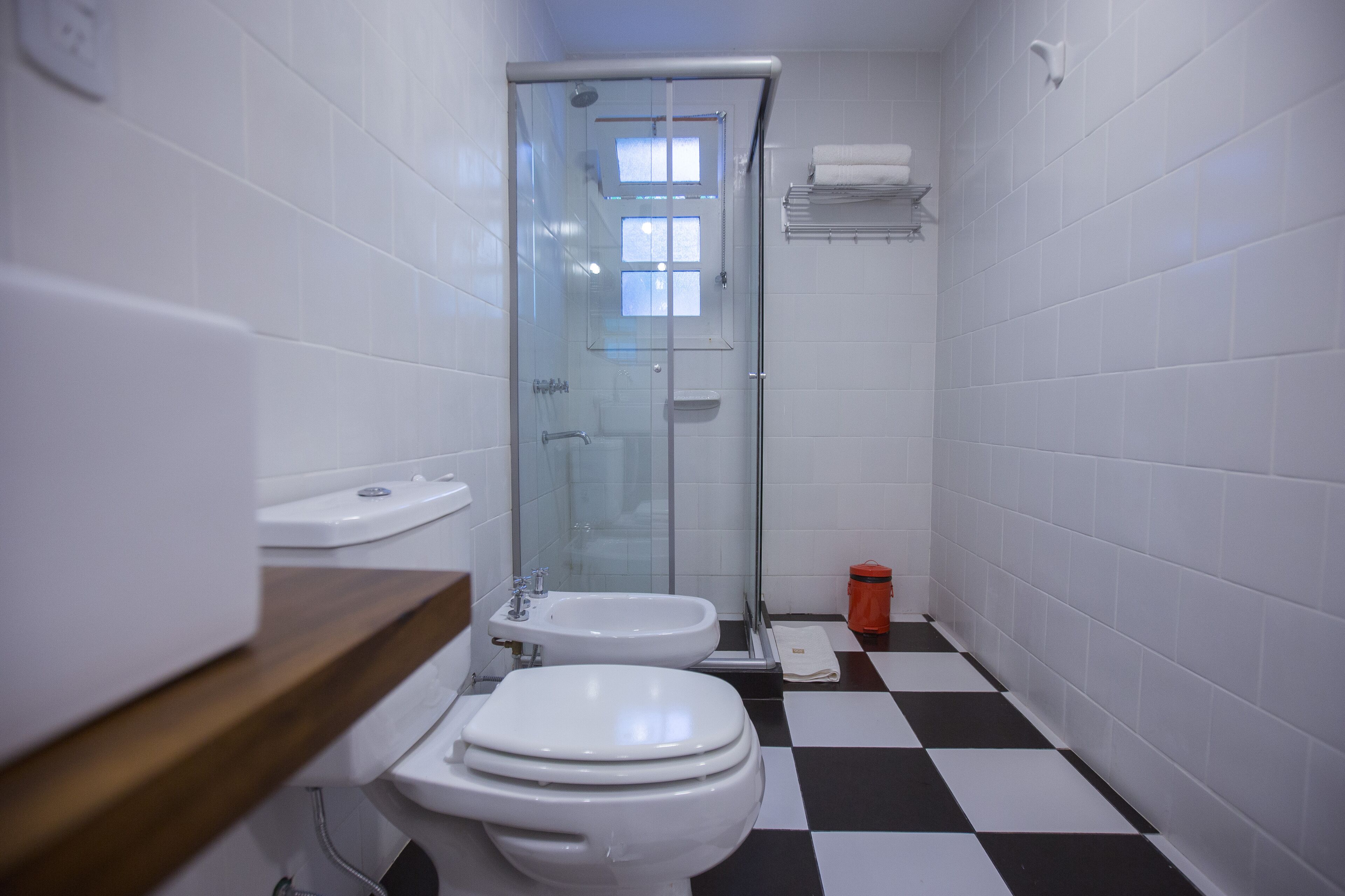 A bathroom with two toilets, a shower, and a checkered floor.