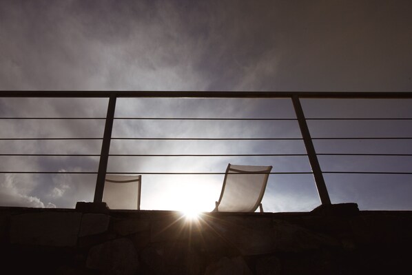 Two chairs positioned on a balcony with a view of the sky and sun.