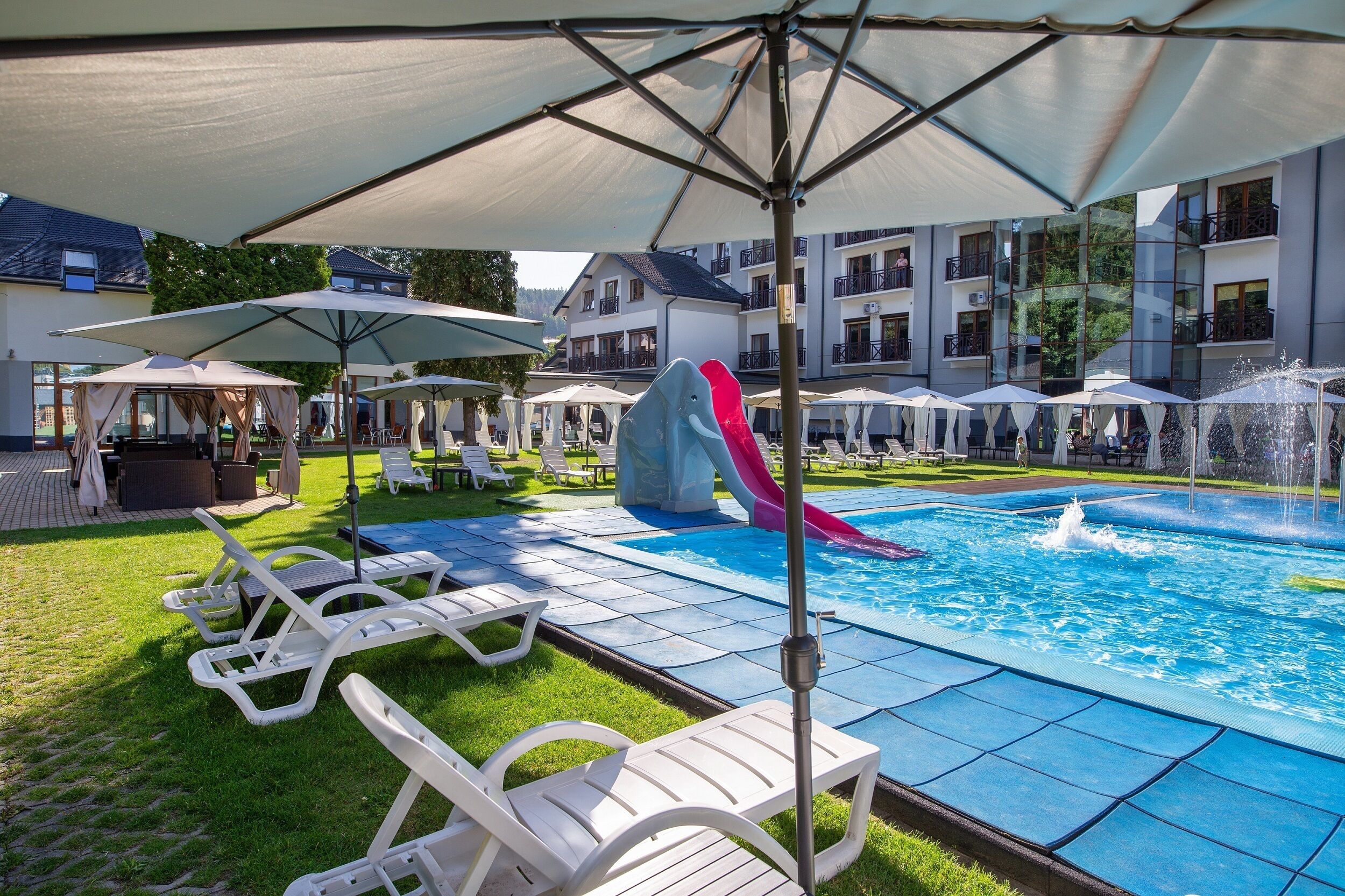 Un área de piscina con sillones reclinables, sombrillas y un tobogán de agua.