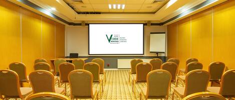 A conference room with rows of chairs, a projection screen, and a podium.