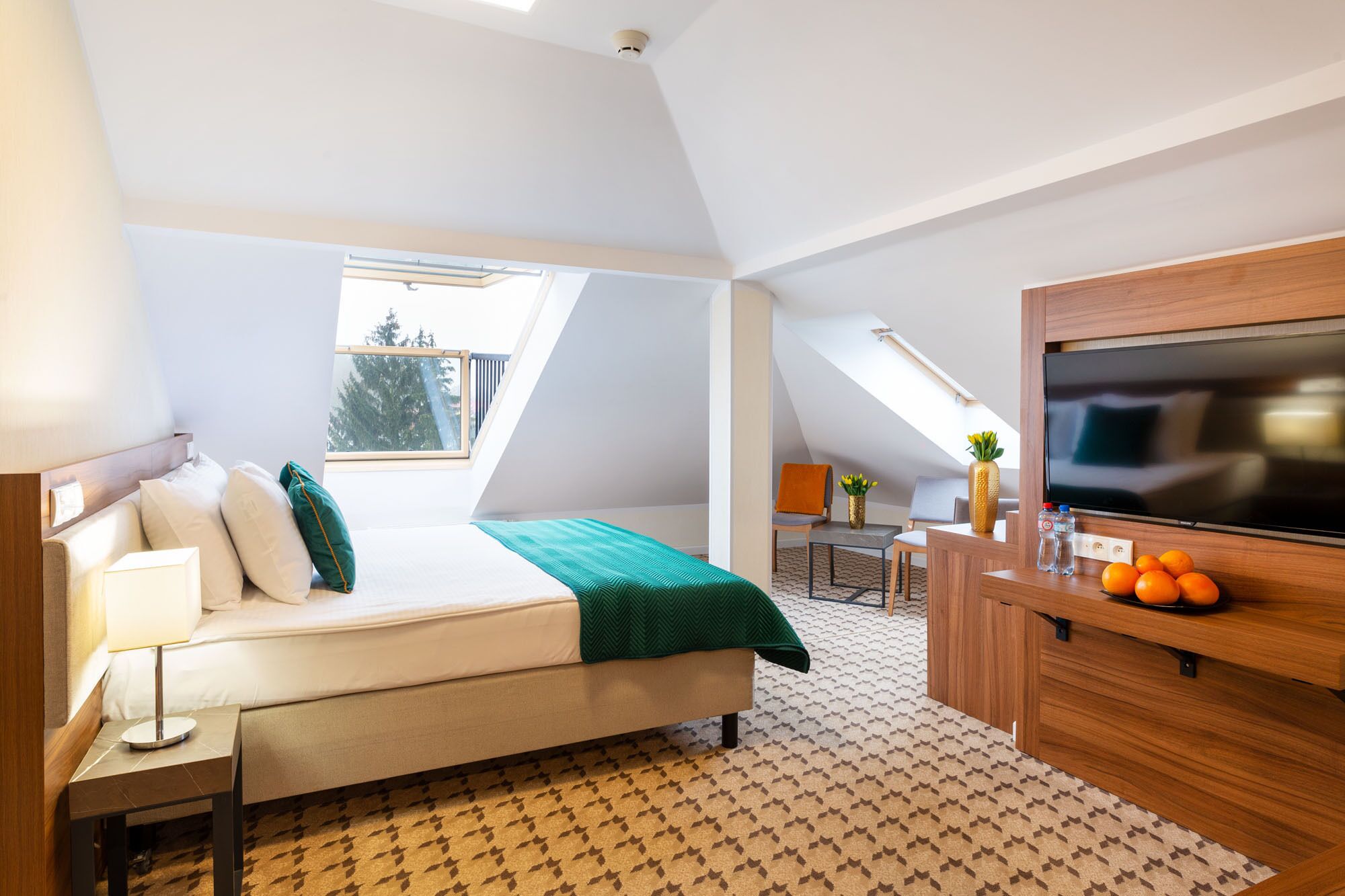 Ett modernt hotellrum med en säng, ett skrivbord, en TV och en liten balkong.